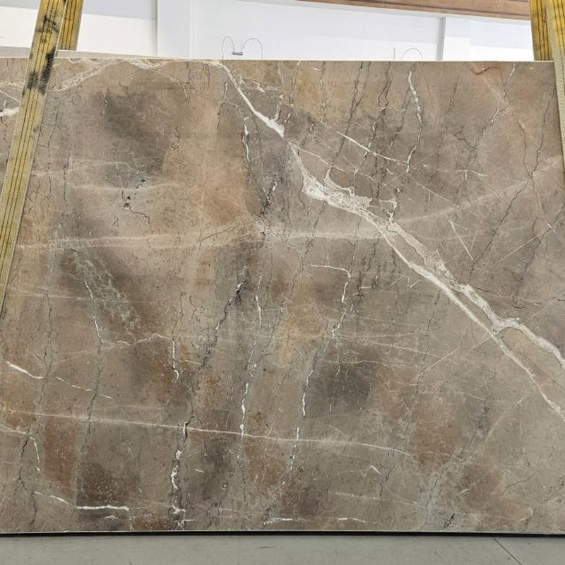 Noisette Fleury marmorplade — varm grå-beige og taupe baggrund med subtile bølgende årer i hvid og mørkegrå poleret finish